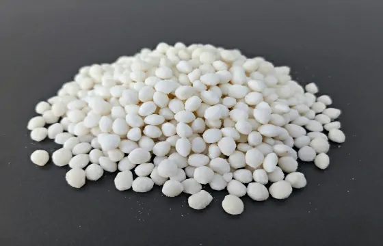 堆积一堆白色颗粒状融雪剂，颗粒多为椭球形、近圆粒状，大小不完全均一，颗粒饱满，堆成低矮料堆，边缘零散散落部分颗粒。